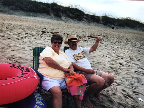 Two people are sitting side by side on beach chairs, smiling and relaxing on the sand.