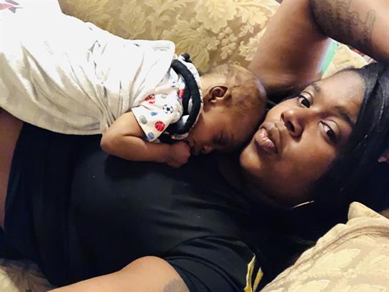 A mother cuddles her sleeping baby on the sofa, radiating love in a cozy atmosphere.