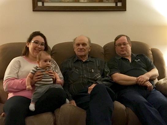 Family members sit on a comfortable couch, smiling and engaging with a baby resting in one lap.