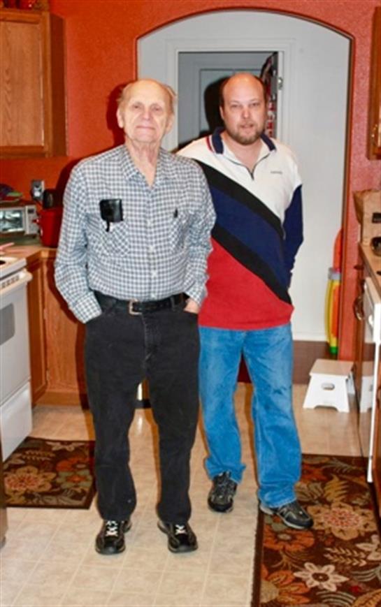 Two men of different ages stand in a warm kitchen, smiling and enjoying each other's company.