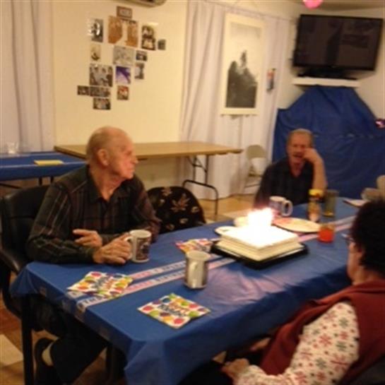 Guests gather around a blue table celebrating a birthday with cake and drinks.