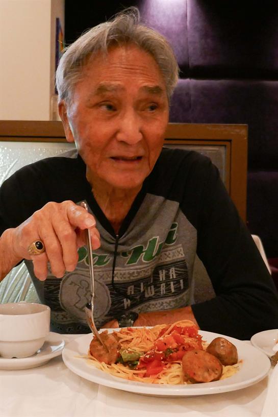 An elderly man smiles while savoring his dinner featuring various dishes and utensils.