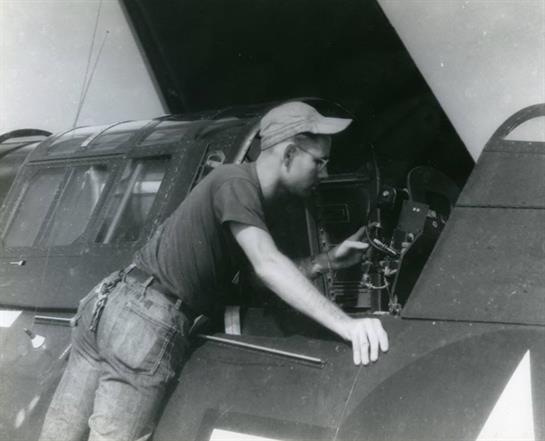 A mechanic inspects the engine of an aircraft in a hanger while wearing a cap and work clothes.
