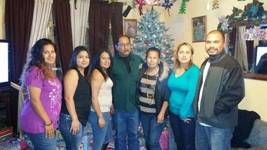 A group of seven people pose together in a warm living room decorated for the holidays.