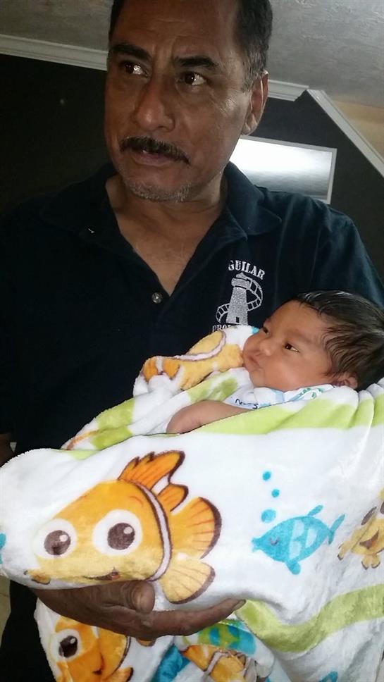A grandfather lovingly cradles his newborn baby wrapped in a colorful blanket at home.