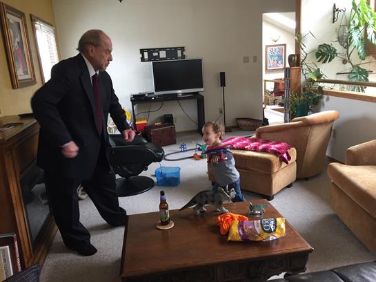 An elderly man in a suit engages in a playful dance with a young child, creating joyful moments.