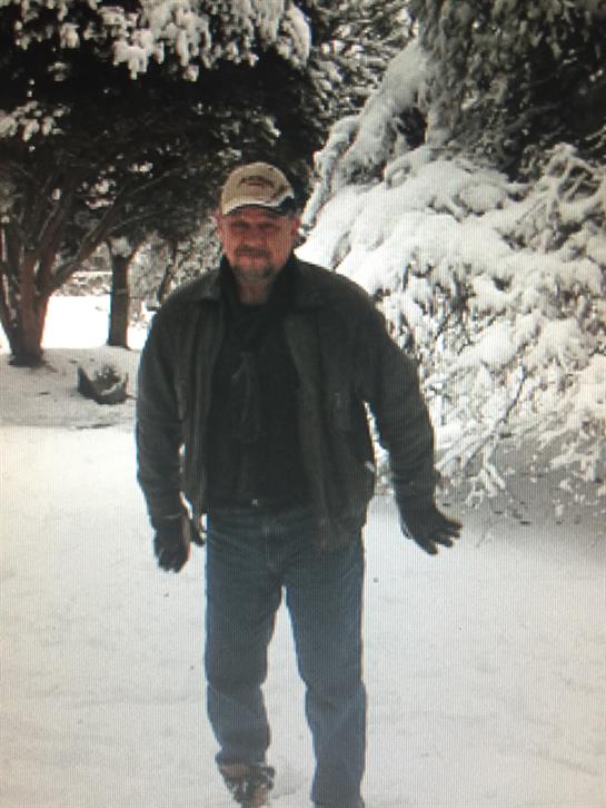 A man stands in deep snow, surrounded by frosted trees, wearing warm clothing and gloves.