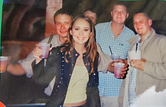 Group of friends smiling and holding drinks together, displaying a cheerful atmosphere.