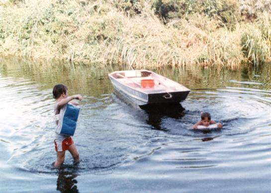 Kids have fun swimming and playing near a boat while enjoying a warm summer day.