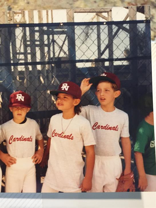 A group of children wearing baseball uniforms stands at a field, enjoying their time together.