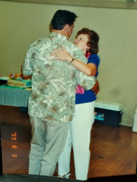 A man and woman embrace while dancing together at a lively community gathering, smiling happily.