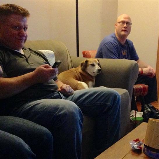 Group of friends relaxing on a couch while watching TV with a dog nearby on a cozy evening.