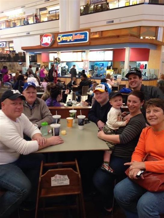 Six family members sit around a table in a bustling food court, sharing laughter and drinks.