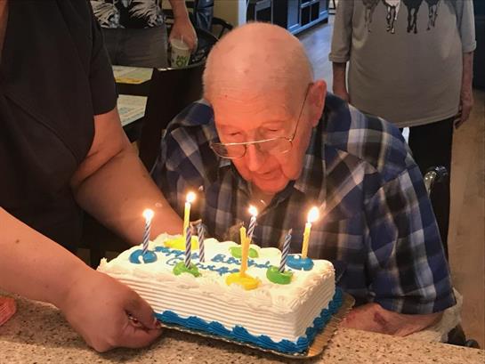 Celebrating a birthday, an older man blows out candles on a decorated cake surrounded by family.