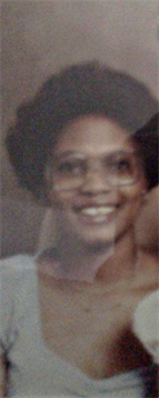 A woman with glasses smiles in a charming, warmly-lit environment decorated with vintage items.