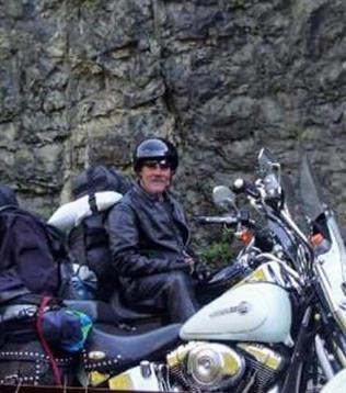 Two motorcyclists take a break beside a rugged rock formation during their adventure in nature.