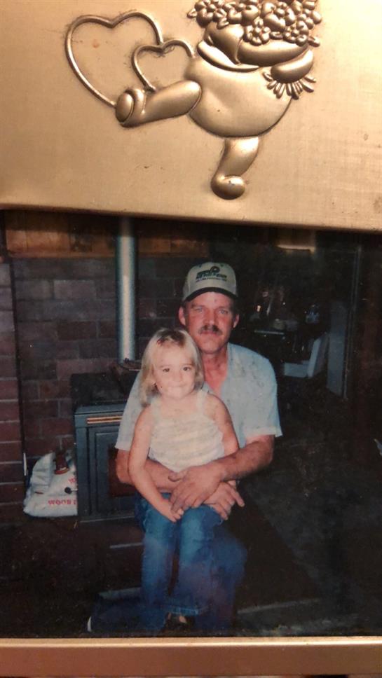 A smiling grandfather holds his young granddaughter on his lap in a warm, inviting living room.