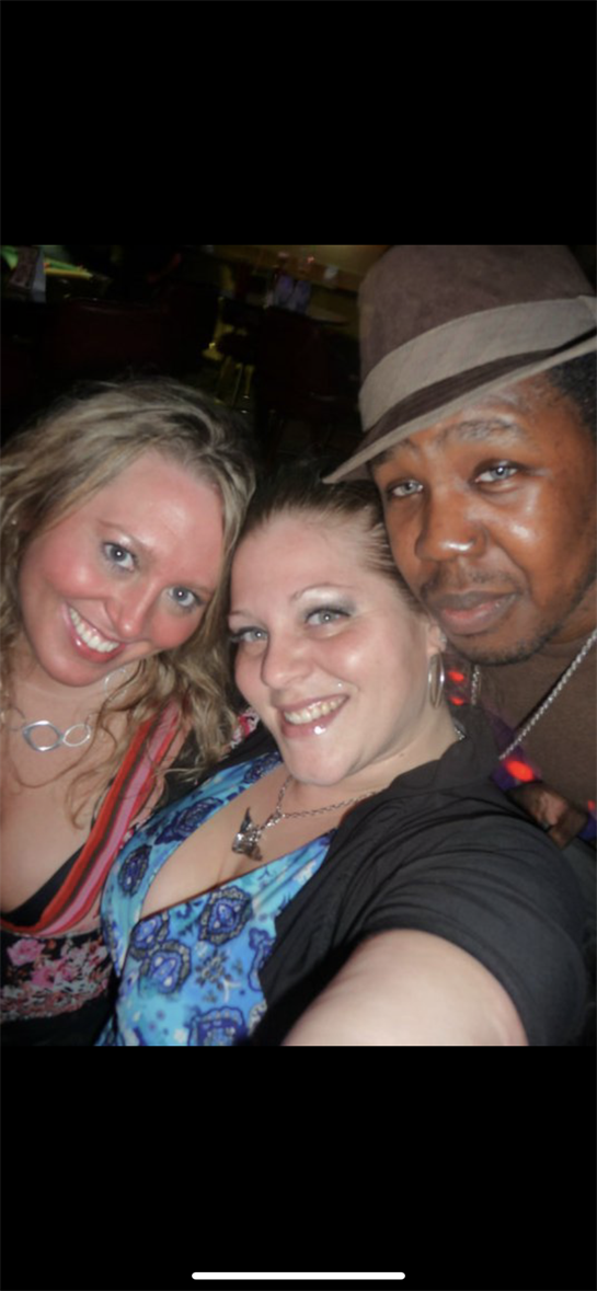 Three friends smile and pose together, capturing a fun moment during a vibrant night out.