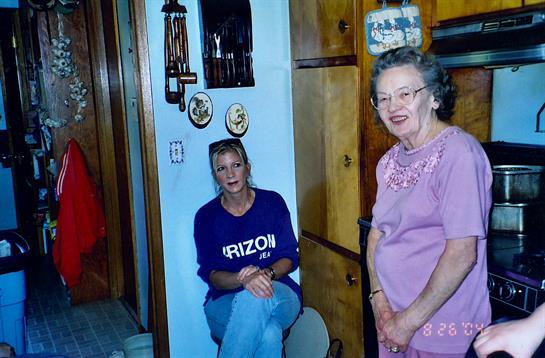 Two women chat in a warm kitchen filled with wooden furnishings and personal decorations.