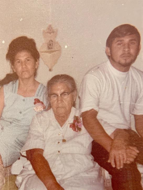 Three family members are seated closely together, sharing smiles and memories in a cozy home.