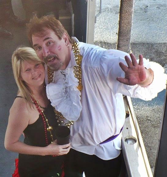 A couple poses for a cheerful photo wearing vibrant costumes with festive accessories at sunset.