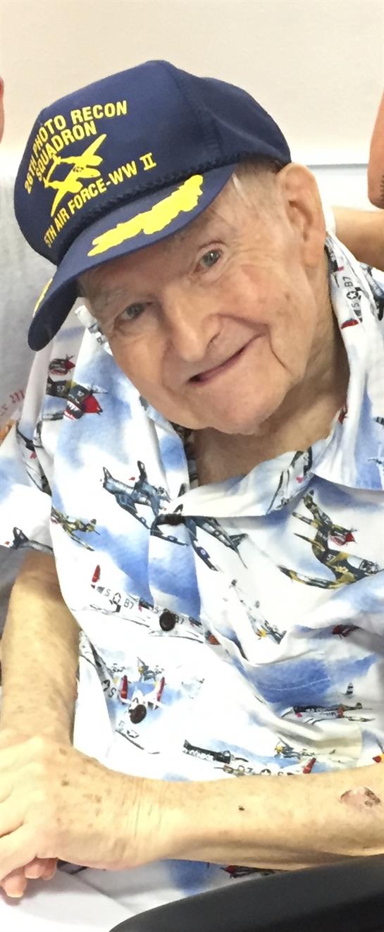 An elderly man enjoys a light-hearted moment, smiling in a vibrant shirt featuring airplane motifs.