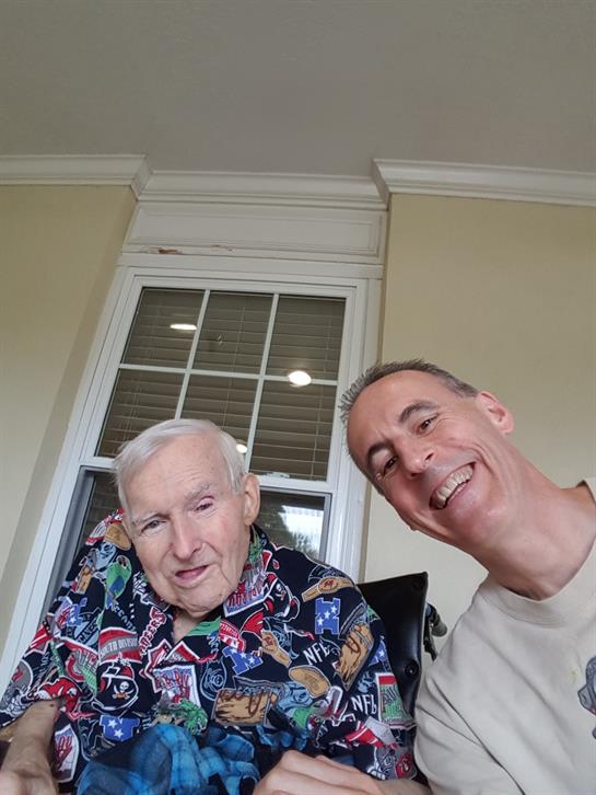 Two men share a joyful moment inside a sunny room filled with warmth and laughter.