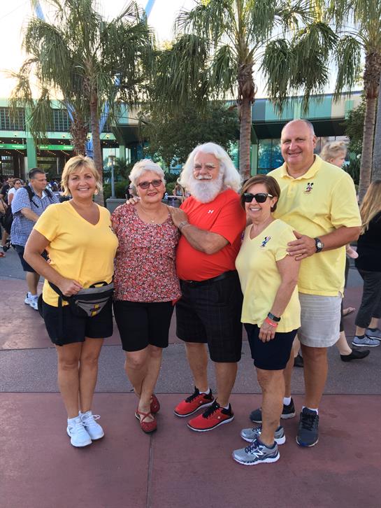 Five friends are smiling and posing together during a sunny day at a fun outdoor gathering.