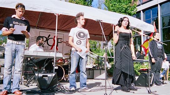 Two performers are on stage singing while a band plays behind them at a lively outdoor event.