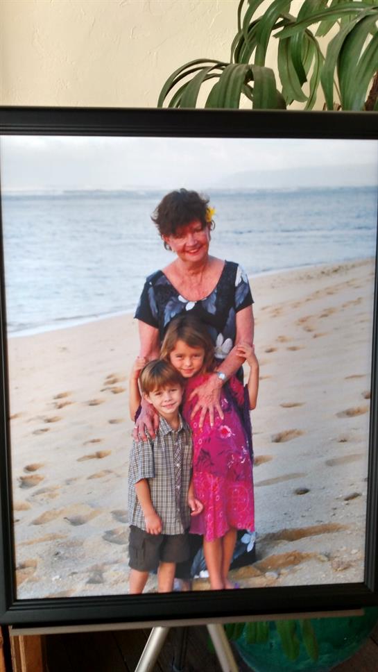 A woman stands with two children on a sandy beach, enjoying a warm day by the water's edge.