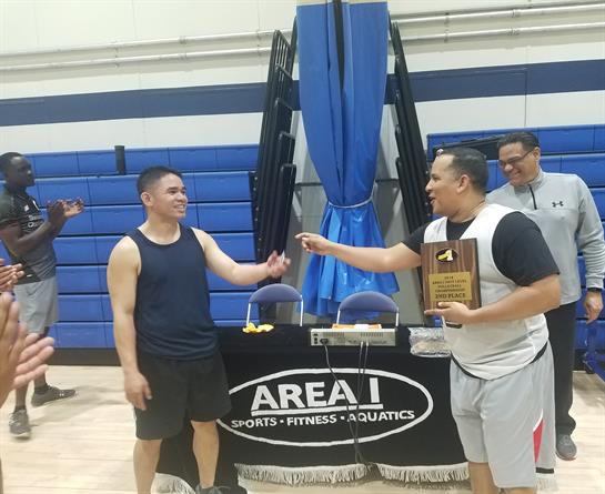 Two players exchange smiles and awards after winning a basketball tournament at a gym.