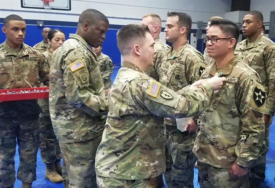 Members of the military are gathered in a gym, receiving awards and recognition for their service.