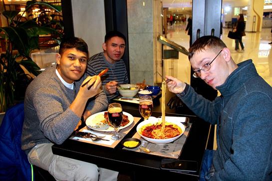 Friends gather around a table, savoring pasta dishes and drinks in a busy restaurant.