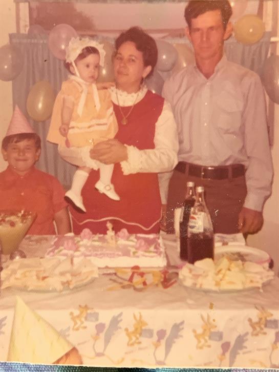 A family gathers around a decorated table with a birthday cake and snacks while celebrating.
