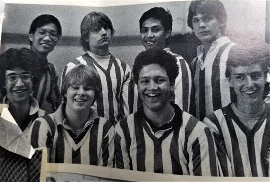 Seven young male athletes smile while wearing striped jerseys during a sports event in the 1980s.