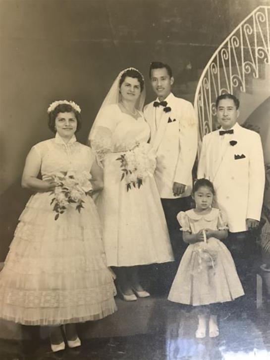 A group of five family members dressed in formal attire celebrates a wedding indoors.