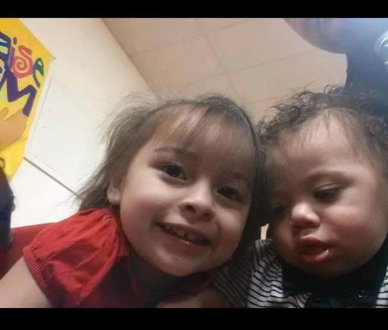 Two children are smiling close together, enjoying their time in a playful indoor setting.