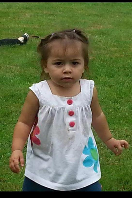 A toddler explores the grassy area with curious expression, dressed in colorful attire.