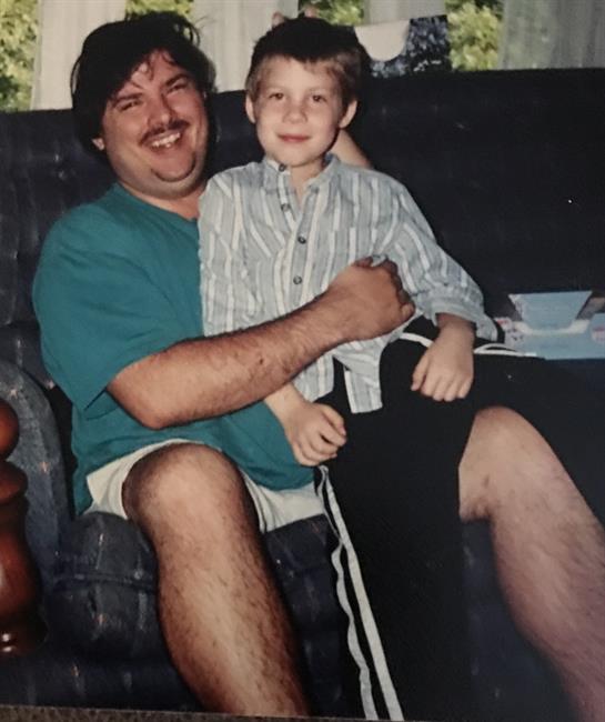 A father smiles while holding his young son on his lap, sharing a joyful moment at home.