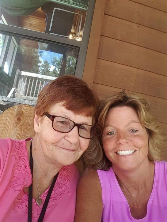 Women relax on a wooden porch, enjoying a warm, sunny day while sharing smiles and conversation.
