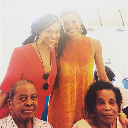 Four family members smile together at a festive gathering on a sunny day outdoors.