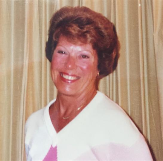A cheerful woman poses with a bright smile, dressed in a white cardigan.