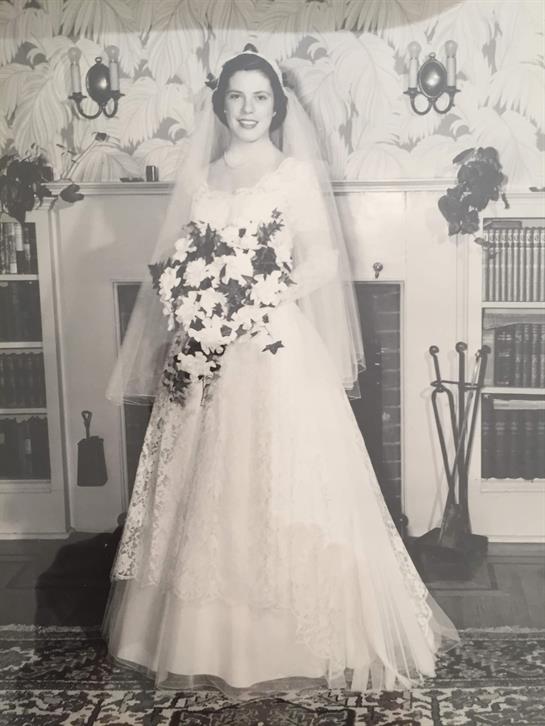 A bride stands proudly in a beautiful wedding dress, holding a bouquet in a decorated room.