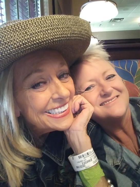 Two women pose joyfully for a selfie, showcasing their friendship in a lively indoor setting.
