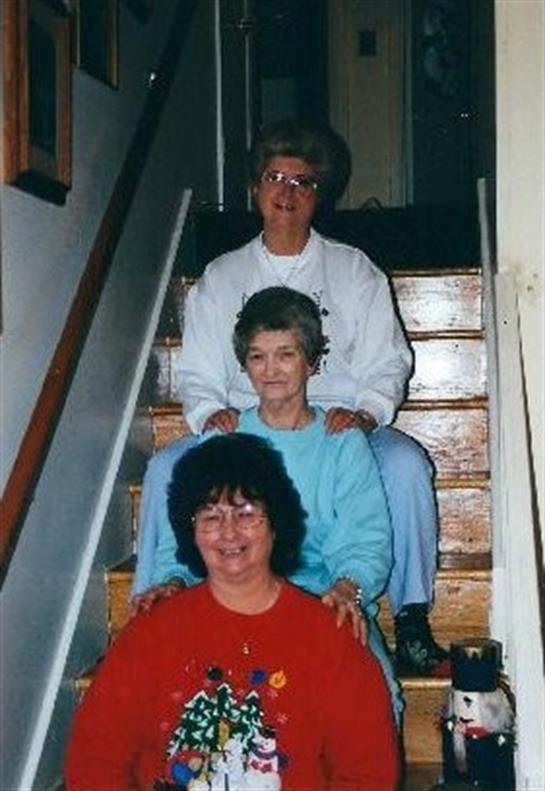 Three women smile warmly while sitting on a staircase, enjoying a moment of togetherness at home.