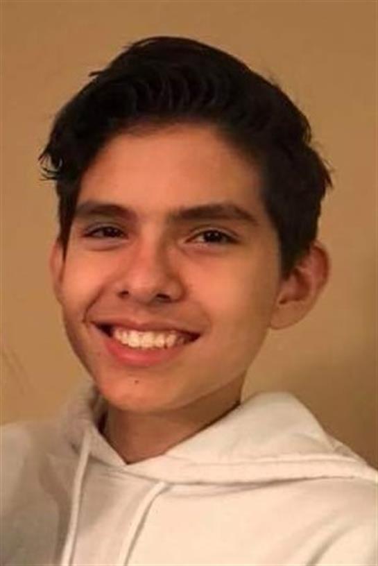 Young boy flashes a bright smile while wearing a light-colored hoodie in a cozy indoor environment.