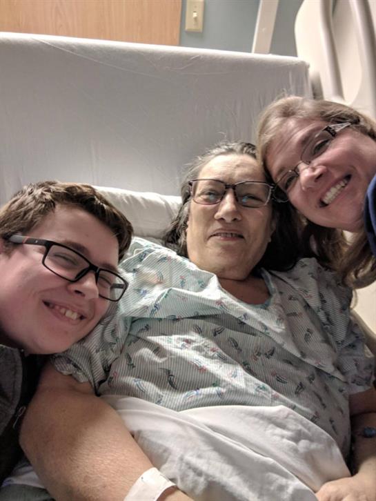 Two family members share a cheerful moment with a patient in a hospital bed during their visit.