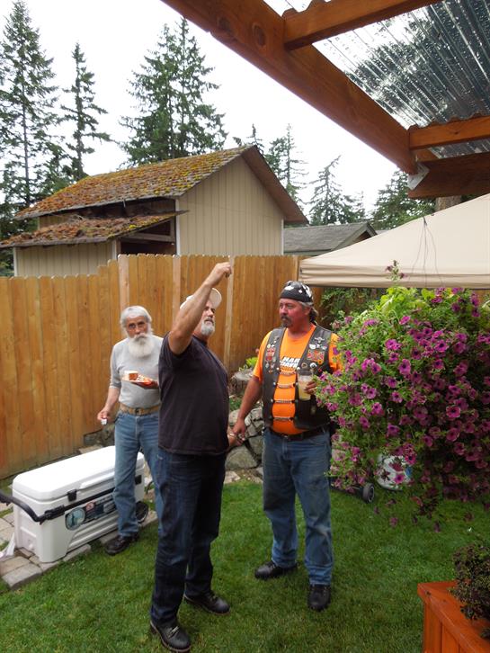 Three men engage in conversation and preparation for a barbecue in a lively backyard setting.