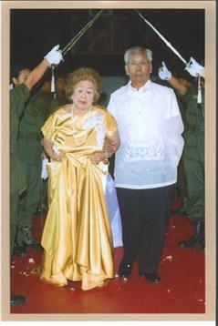 A well-dressed couple walks down a red carpet while military personnel display ceremonial swords.