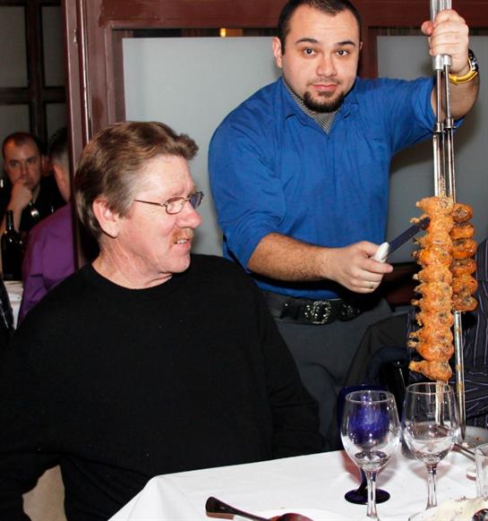Guests at a restaurant enjoy a Brazilian barbecue as a waiter serves skewers of meat.